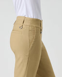 Close-up side view of a person wearing tan chaps-style pants with a white top, showing the waistband, belt loops, front pocket, and fabric texture against a light gray studio background.