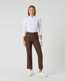 A woman modeling a white long-sleeve polo shirt and brown straight-leg trousers, paired with white gloves and white sneakers, against a light gray studio background.