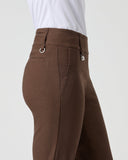 A side profile view of a person wearing brown riding breeches with a white shirt, shown against a light gray studio background.