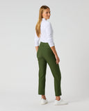 A woman wearing olive green cropped trousers, a white long-sleeve top, and white sneakers, standing in profile against a light gray studio background.