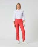 A woman modeling a white long-sleeve polo shirt and bright coral-red cropped pants, standing against a light gray studio background.