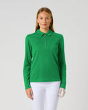 A woman modeling a bright green long-sleeve polo shirt with a half-zip collar, paired with white pants, against a plain light gray studio background.