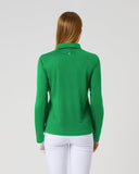A woman viewed from behind wearing a bright green long-sleeve polo shirt and white pants against a plain light gray studio background.