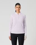A woman modeling a light lavender long-sleeve athletic polo shirt with a half-zip collar, paired with black leggings, against a solid light gray background.