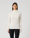 A woman modeling a ribbed long-sleeve mock neck top in off-white, paired with black leggings and white gloves, against a light gray studio background.