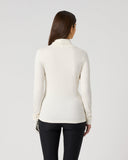 A woman viewed from behind wearing a fitted cream mock-neck long-sleeve top and black pants, standing against a plain light gray studio background.
