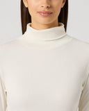 A woman wearing a cream-colored ribbed mock neck long-sleeve top, shown from the chest up against a light gray studio background.