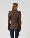 A woman viewed from the back wearing a brown ribbed long-sleeve mock neck top and dark navy pants, standing against a light gray studio background.
