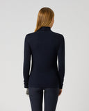 A woman with blonde hair is shown from the back wearing a dark navy long-sleeve mock neck top and matching dark pants against a light gray studio background.