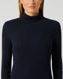 A woman wearing a dark navy ribbed long-sleeve turtleneck top, shown from the nose down against a light gray studio background.