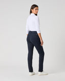 A woman is shown from the back wearing a white mock-neck long-sleeve top, navy blue slim-fit trousers, and white sneakers, standing against a light gray studio background.