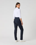 A woman is shown from the back wearing a white mock-neck long-sleeve top, navy blue slim-fit trousers, and white sneakers, standing against a light gray studio background.