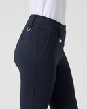 Close-up side view of a person wearing dark navy equestrian riding pants with a white shirt tucked in, against a light gray studio background.