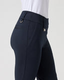 Close-up side view of a person wearing dark navy equestrian riding pants with a white shirt tucked in, against a light gray studio background.