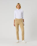 A woman modeling a white long-sleeve golf polo and beige slim-fit golf pants with white golf shoes, standing against a light gray studio background.