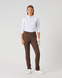 A woman modeling a white long-sleeve polo shirt and brown slim-fit trousers, paired with white gloves and white sneakers, against a light gray studio background.