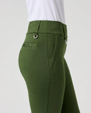 A close-up side view of a model wearing olive green riding breeches with a white top, set against a plain light gray studio background.