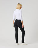 A woman with blonde hair is shown from behind wearing black slim-fit pants, a white long-sleeve top, and white sneakers, standing against a light gray studio background.