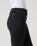 Close-up side view of a person wearing black riding breeches with a white shirt, showing the waistband, belt loops, side pocket, and leg fit against a light gray studio background.