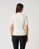 A woman viewed from behind wearing a short-sleeve ribbed knit top in off-white and black leggings, standing against a plain light gray studio background.