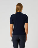 A woman viewed from the back wearing a dark navy ribbed short-sleeve mock-neck top and matching dark navy leggings against a light gray studio background.