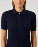 A woman wearing a navy blue short-sleeve polo shirt with a textured cable knit pattern, shown from the chest up against a light gray studio background.