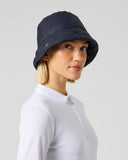 A woman wearing a dark navy blue bucket hat and a white long-sleeve cycling jersey, shown from the side against a light gray studio background.