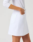 A white tennis skirt with a side pocket, shown on a model wearing a white long-sleeve top against a light gray studio background.