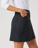 A person wearing a black A-line mini skirt with a side pocket, paired with a white long-sleeve top, shown from the waist down against a light gray studio background.