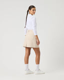 Person wearing a white shirt and beige skirt on a plain background