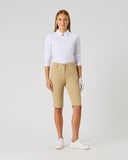 A woman modeling a white long-sleeve polo shirt and beige fitted riding shorts with white golf shoes, standing against a light gray studio background.