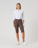 A woman modeling a white long-sleeve polo shirt and brown golf shorts with white golf shoes, standing against a light gray studio background.