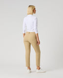 A woman with blonde hair is shown from the back wearing beige cropped trousers, a white long-sleeve top, and white sneakers against a light gray studio background.
