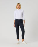 A woman modeling a white long-sleeve half-zip polo shirt and dark navy cropped trousers, paired with white sneakers, against a light gray studio background.