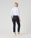 A woman with blonde hair is shown from behind wearing a white long-sleeve mock neck top, dark navy cropped trousers, and white sneakers, standing against a light gray studio background.