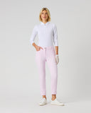 A woman modeling light pink slim-fit pants, paired with a white long-sleeve polo shirt, white gloves, and white sneakers, standing against a light gray studio background.
