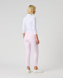 A woman with blonde hair is shown from behind wearing light pink slim-fit pants, a white long-sleeve mock neck top, and white sneakers, standing against a light gray studio background.