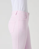 A side profile view of a model wearing light pink equestrian riding pants and a white textured shirt, set against a plain light gray studio background.