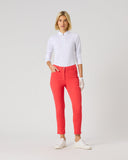 A woman modeling bright coral-red slim-fit pants, paired with a white long-sleeve polo shirt, white gloves, and white sneakers, standing against a light gray studio background.