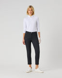 A woman modeling a white long-sleeve polo shirt and dark charcoal gray cropped pants, paired with white sneakers and a white glove, against a light gray studio background.