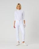 A woman modeling a white long-sleeve mock-neck top and white skinny jeans with white sneakers, standing against a light gray studio background.