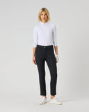 A woman modeling slim-fit black trousers, paired with a white long-sleeve polo shirt and white sneakers, standing against a solid light gray studio background.