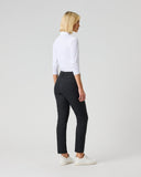 A woman with blonde hair is shown from the back wearing black slim-fit trousers, a white long-sleeve top, and white sneakers, standing against a light gray studio background.