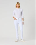 A woman modeling a white long-sleeve polo shirt and matching white trousers, standing against a plain light gray studio background.