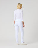 A woman with blonde hair is shown from behind wearing a white mock-neck long-sleeve top, white skinny jeans, and white sneakers against a light gray studio background.