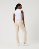 Woman wearing a white sleeveless top and beige pants on a plain background