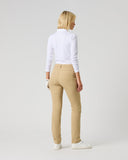 A woman is shown from behind wearing beige slim-fit trousers, a white long-sleeve top, and white sneakers, standing against a light gray studio background.