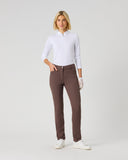 A woman modeling slim-fit brown trousers, paired with a white long-sleeve polo shirt and white gloves, standing against a light gray studio background.