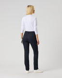 A woman is shown from the back wearing slim-fit navy trousers, a white long-sleeve top, and white sneakers against a light gray studio background.