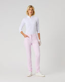 A woman modeling light pink slim-fit pants with a white long-sleeve polo shirt and white sneakers, standing against a light gray studio background.